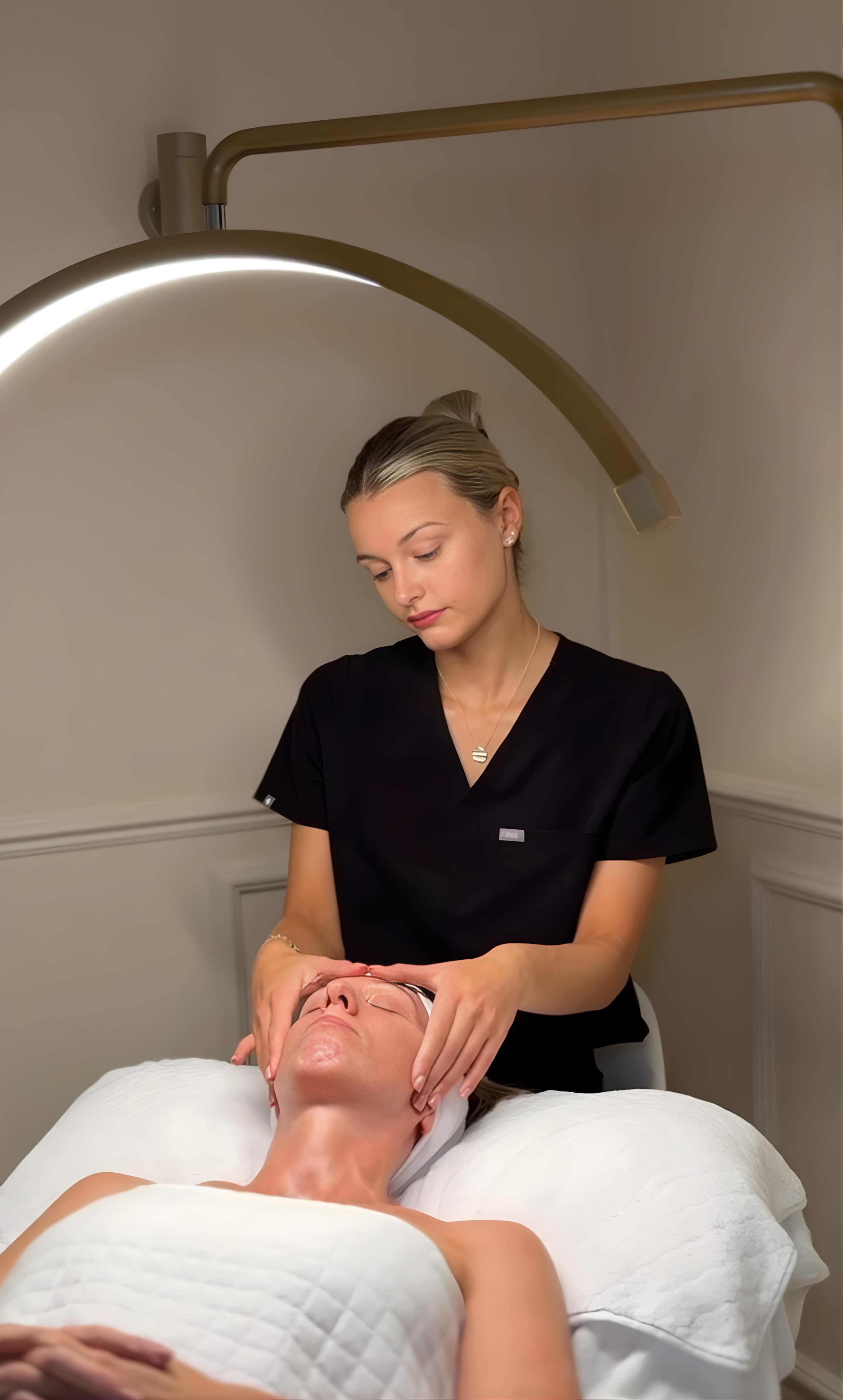Woman providing a facial massage to another person in a clinical setting.